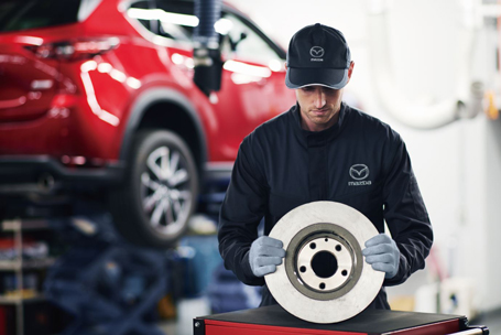 Mazda technician holds a brake disc in the workshop, highlighting Mazda safety checks, Mazda service care, and quality.